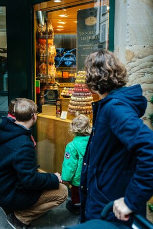 Strasbourg, France - Dec 27, 2017: Woman looking at single father with two daughters admiring the bakery showcase window with French macarons cakeのeditorial素材