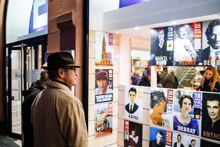 Strasbourg, France - Dec 27, 2017: Side view of beautiful adult man wearing classic hat reading diverse bookstore announcement with writers arriving to sing booksのeditorial素材
