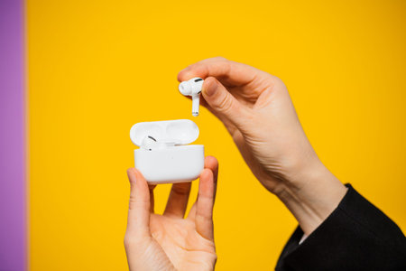 Paris, France - Oct 30, 2019: Woman hands unboxing new Apple Computers AirPods Pro headphones with Active Noise Cancellation for immersive sound - charging case yellow backgroundのeditorial素材