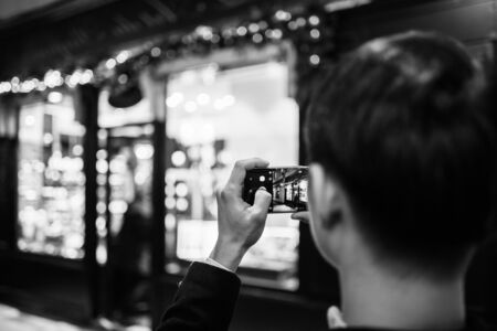 Strasbourg, France - Nov 23, 2017: Rear view of adult man taking photographs of the illuminated and decorated showcase entrance of French traditional store in Christmas Market capital - black and white imageのeditorial素材