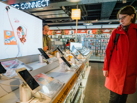 Nice, France - Nov 24, 2019: Woman in red coat looking inside electronics Fnac store at multiple...