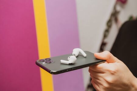 Paris, France - Oct 30, 2019: Side view of woman hands holding new Apple Computers AirPods Pro headphones with Active Noise Cancellation for immersive sound on top of iPhone 11 Pro smartphoneのeditorial素材