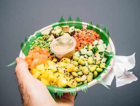 Man hand holding against gray background Poke Bowl with fresh bio organic Japanese saladの写真素材
