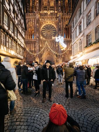 Strasbourg, France - Dec 24, 2018: Wide angle lens over Rear view of woman wearing red beret hat taking a memory photo of her boyfriend in front of the Notre-Dame de Strasbourg catherdral Christmas Marketのeditorial素材