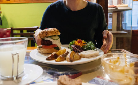 Woman eating delicious burger with vegetables in cozy restaurant in Barcelona, Spain