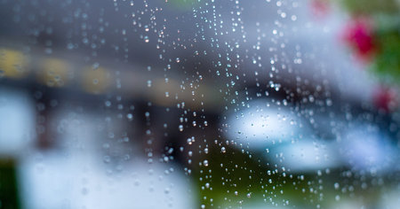 Close-up of glass window surface with rain drops on the outside and defocused leaves of a tree