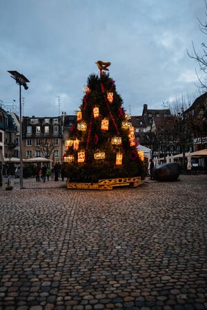 Strasbourg, France - Dec 24, 2018: Pedestrians - locals and tourists sightseeing the small decorated with toys Christmas tree in small square in central Strasbourg during annual Christmas Marketのeditorial素材