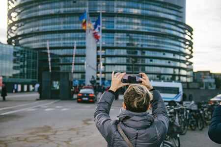 Strasbourg, France - Dec 17, 2019: Elevated view of woman taking a photograph on the smartphone of the European Parliament building symbol of freedom and rule of law in European Unionのeditorial素材
