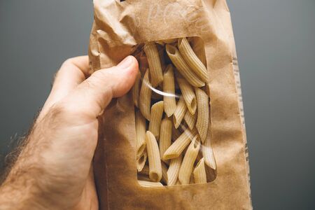 Man hand holding against gray background bio organic authentic artisanal pasta from durum wheat semolinaの写真素材