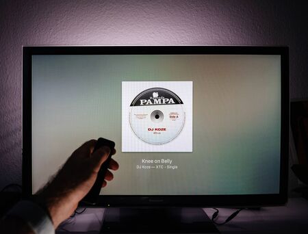 Paris, France - Circa 2019: Man surfing with remote Apple TV menu on Panasonic Plasma tv living room loading message of Apple Music streaming service Dj Koze new singleのeditorial素材