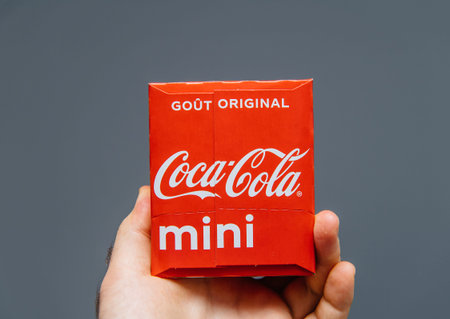 Paris, France - Jul 20, 2019: Man hand holding against gray background pack of Coca-Cola sweet drink...