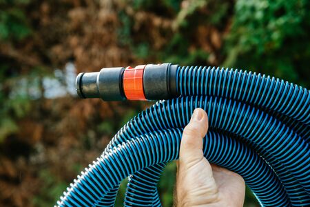 Professional worker male hand holding showing against green garden background new blue anti static vacuum hose for a professional tool vacuum cleanerの写真素材
