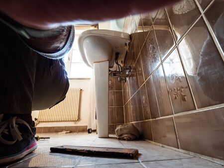Low angle view of adult male plumber working repairing disassembling old vintage sink in old bathroomの写真素材