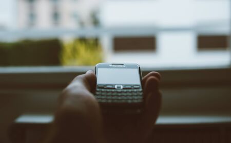 London, United Kingdom - Apr 21, 2013: Vintage film over POV male hand holding in palm vintage Blackberry professional smartphone with focus on the logotype with the tilt-shift lens and large window in backgroundのeditorial素材