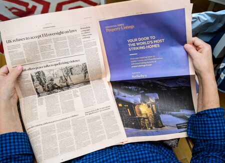 Paris, France - Feb 19, 2020: POV of senior hands holding latest Financial Times newspaper reading the Property Listing advertising supported by Sothebys and other economic and financial articlesのeditorial素材