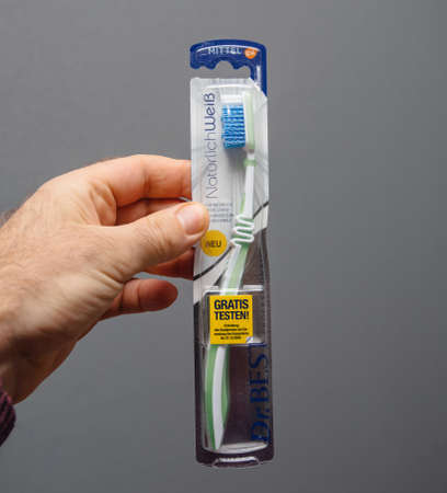 Paris, France - Mar 5, 2020: Square image POV male hand holding Dr Best toothbrush against gray background with large yellow Gratis testen German stickerのeditorial素材