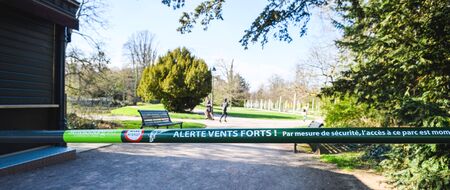 Closed French park with steel barrier and signage text Closed due to strong winds - French parks are closed during Coronavirus outbreak disease people running in backgroundの写真素材
