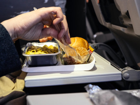 Woman holding fork and knife eating delicious meal in modern aircraft economy business class during...