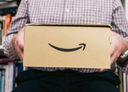 Paris, France - April 2, 2019: Senior male hands holding in living room new delivered parcel from Amazon Prime e-commerce site online shoppingのeditorial素材