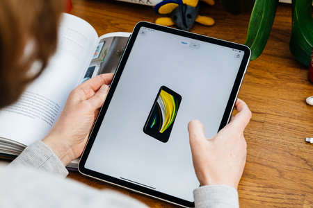 Paris, France - Apr 16, 2020: Woman looking on Apple Computers internet website on iPad Pro tablet in room environment showcasing new iPhone SE withのeditorial素材