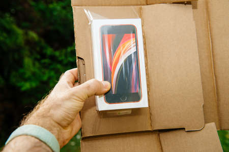 Paris, France - Apr 24, 2020: Man hodling parcel with new budget iPhone SE by Apple Computers touch ID, Single-lens rear camera and iPhone 8 design with internals from 11 Pro versionのeditorial素材