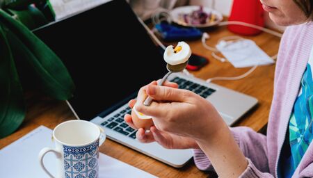 Side view of a lonely woman working from home eating a boiled egg during her teleworking session - worldwide epidemy of Coronavirus COVID19 has put people in lockdown and tele workingの写真素材