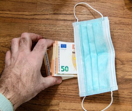 Man putting money 50 euros bank notes under surgical procedure medical face mask during Coronavirus worldwide shortage of masks - as demand during quarantine in US, Europe, Asia during global pandemicの写真素材