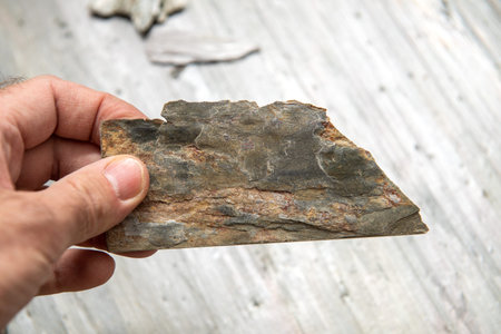 POV Man hand holding natural slate - part of a damaged tile