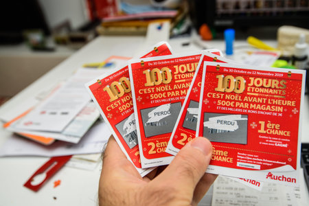 Paris, France - Nov 15, 2019: Man hand holding scratched lottery coupons tickets from Auchan Supermarkets with Perdu Lost sign under a protective layerのeditorial素材