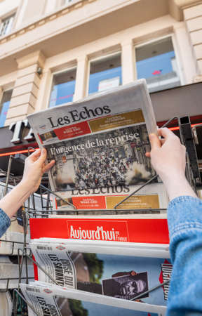 Paris, France - May 30, 2020: Woman wearing mask buying at press kiosk Les Echos economic newspaper featuring cover image with shopping pedestrian street and title urgency of reopeningのeditorial素材