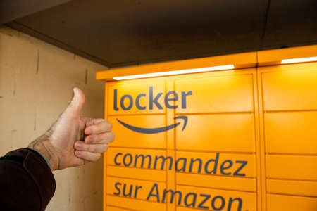 Haguenau, France - April 2, 2020: Male hand thumb-up in front of Amazon Locker with large advertising inscription to order on Amazonのeditorial素材