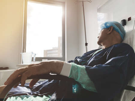 Lying on the medical chair senior male inside modern hospital in France resting after infection virus coronavirus - large window of hope with sunflareの写真素材
