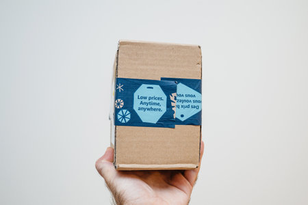 Paris, France - Dec 12, 2020: POV male hand holding parcel package from Amazon Prime with Low Price Anytime, Anywhere advertising on the package - isolated on whiteのeditorial素材