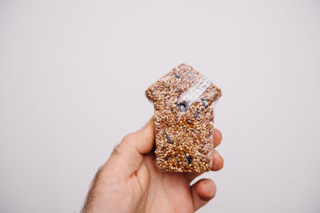 Man hand holding seeds for birds in the shape of a house against a white background