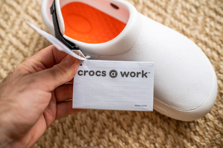 Paris, France - Dec 13, 2020: POV male hand holding paper advertising tag of Crocs at work...