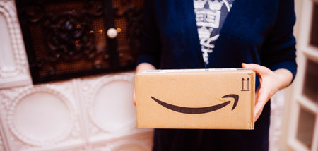 Paris, France - Dec 13, 2020: Hands of elegant woman holding as a gift an Amazon Prime parcel with its arrow smiling logotype with luxury stove in backgroundのeditorial素材
