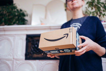 Paris, France - Dec 13, 2020: Side view of elegant woman holding as a gift an Amazon Prime parcel with its arrow smiling logotype with luxury stove in backgroundのeditorial素材