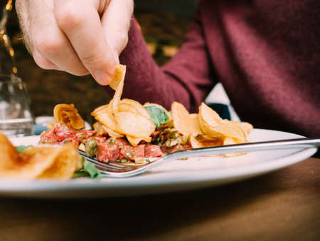 Close-up image of male hand eating from the plate potatoes chips with veal meat and salad - delicious meal in restaurant cafeの写真素材