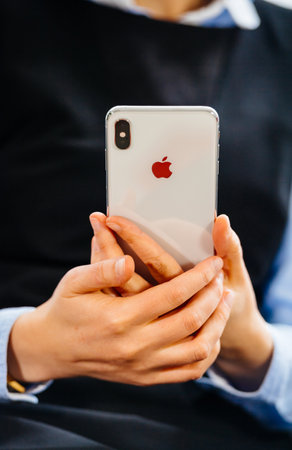 Paris, France - Oct 2, 2018: Close-up business woman hodling new Apple Computers iPhone smartphone normal - focus on hands with logotype of the back of glass phoneのeditorial素材