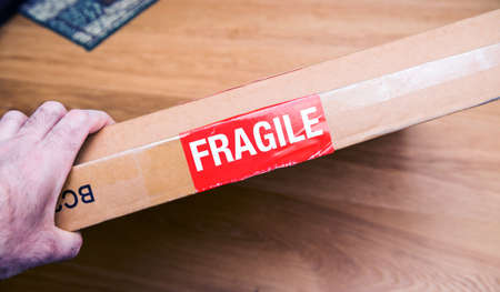 Fragile signage on the cardboard box of a new parcel delivered by freight transportation service pov male hand holding the boxの写真素材