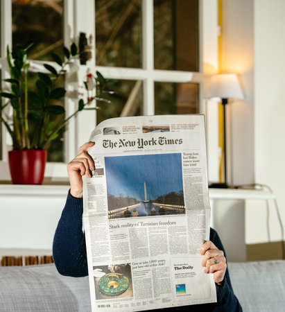 PARIS, FRANCE - JAN 21, 2021: Woman reading The New York Times newspaper featuring breaking news and headlines with Joe Biden inauguration as the 46th President of the United States and Kamalla Harrisのeditorial素材
