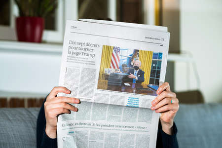 Paris, France - Jan 21, 2021: Woman reading Le Monde newspaper with title changing Trump orders by Joe Biden - as the newly elected US President sworn in as the 46th President of United Statesのeditorial素材