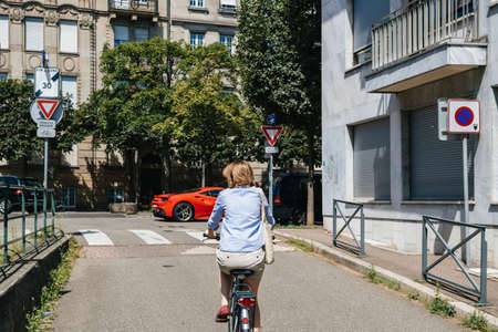 Strasbourg, France - - July 29, 2017: Rear view of single woman cycling on the French street with red ferrari car parked in frontのeditorial素材