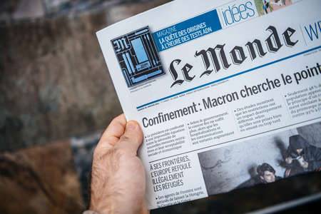 London, United Kingdom - FEb 2, 2021: POV male hand holding reading French Le monde newspaper with lockdown confinement and Macron seeking solutions headlinesのeditorial素材