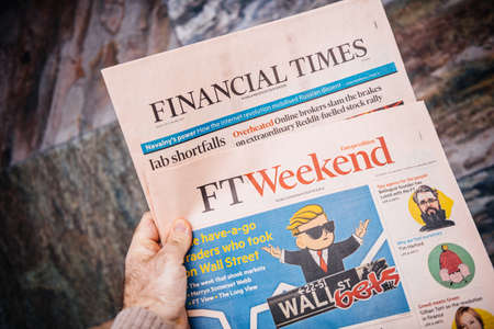 London, United Kingdom - FEb 2, 2021: POV male hand holding Financial Times FT weekend newspaper reading about the Wall Street bets trades on a Reddit forumのeditorial素材
