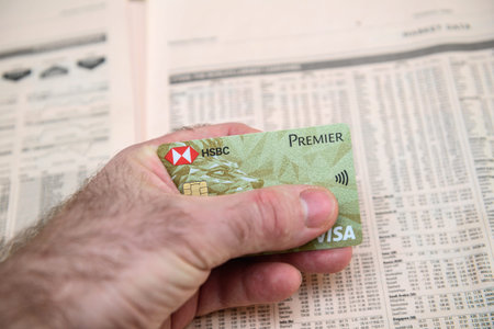 Paris, France - FEb 13, 2021: POV business man holding gold luxury HSBC premier visa credit debit card against stock quotations of diverse companies on pages of Financial TImes newspaperのeditorial素材