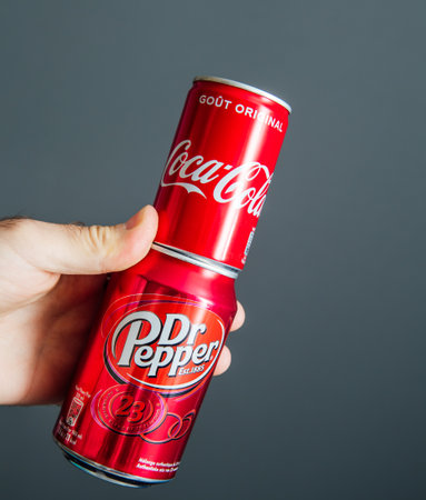 Paris, France - May 3, 2020: POV male hand holding aluminum can of Coca Cola and Dr Pepper manufactured by Dr Pepper Snapple Group soft sweet drinks - isolated against gray backgroundのeditorial素材
