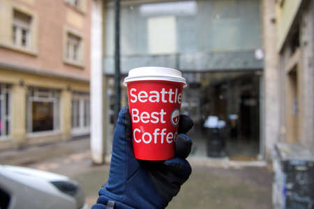 Strasbourg, France - Jan 14, 2021: POV male hand wearing winter glove personal perspective holding plastic paper cup with Seattle best Coffee logotypeのeditorial素材
