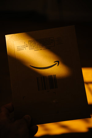 Paris, France - FEb 13, 2021: POV male hand holding new parcel from Amazon Prime ecommerce website with ray of sun on the arrow smiling logotypeのeditorial素材