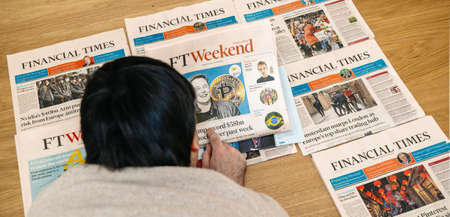 Paris, France - Feb 13, 2021: Overhead view of young man reading on the wooden floor multiple Financial Times newspapers with diverse headlines with Elon Musk and bitcoin cryptocurrencyのeditorial素材